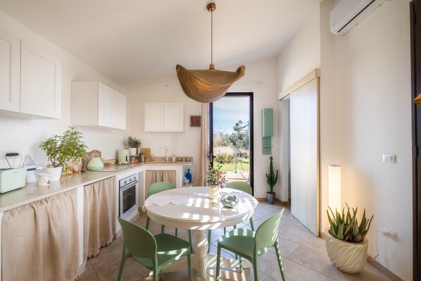 A kitchen with a round table, chairs, a hanging light fixture, cabinets, a stove, and a potted plant.
