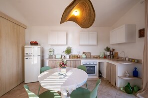 A compact kitchen with a dining table, chairs, a refrigerator, an oven, and a unique pendant light.