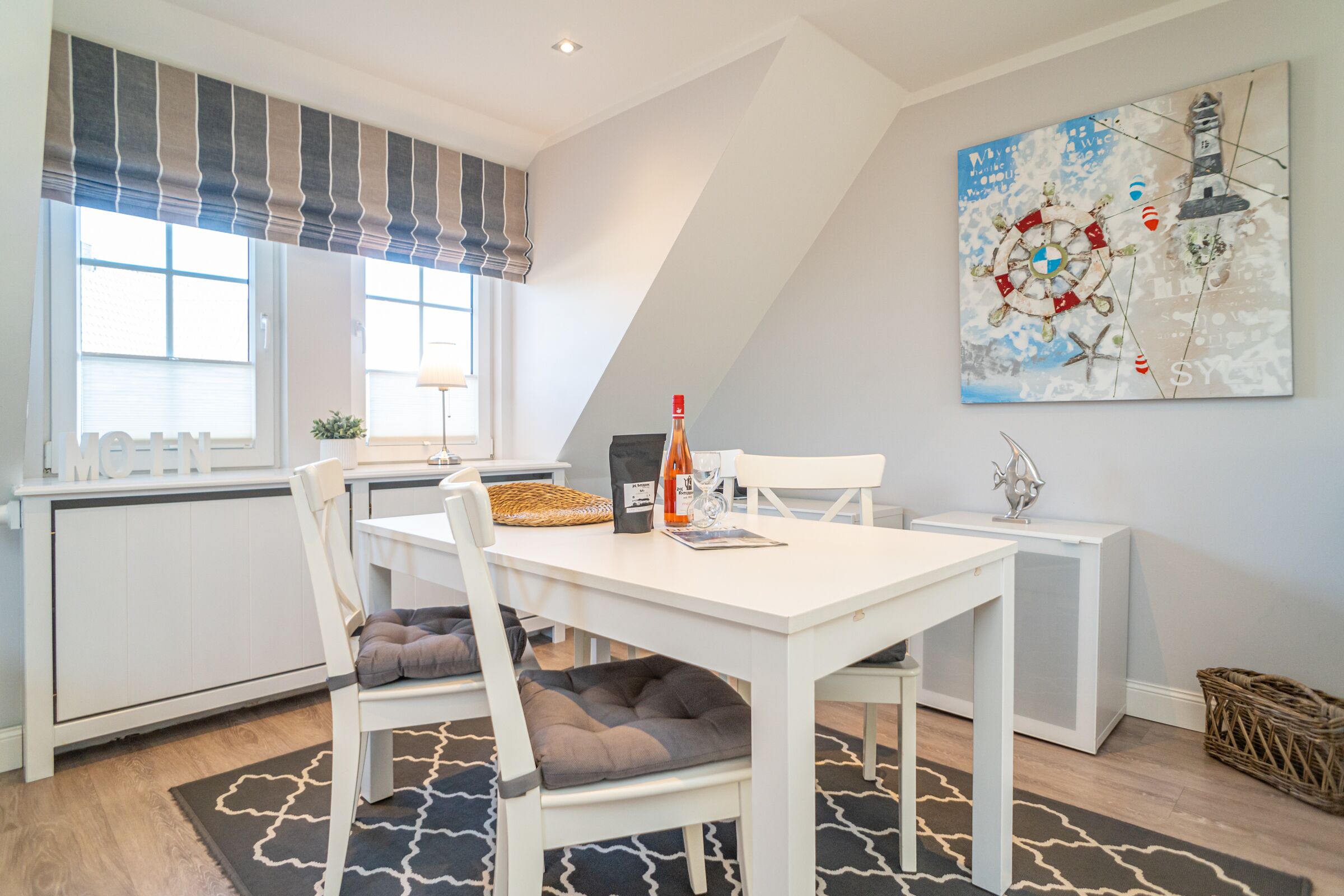 A dining area with a white table and chairs, a bottle of wine, and a painting on the wall.