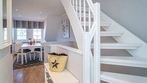 A modern interior with a staircase, a dining area with a table and chairs, and a basket on a bench. - Appartement Dünenglück (Wenningstedt-Braderup (Sylt))