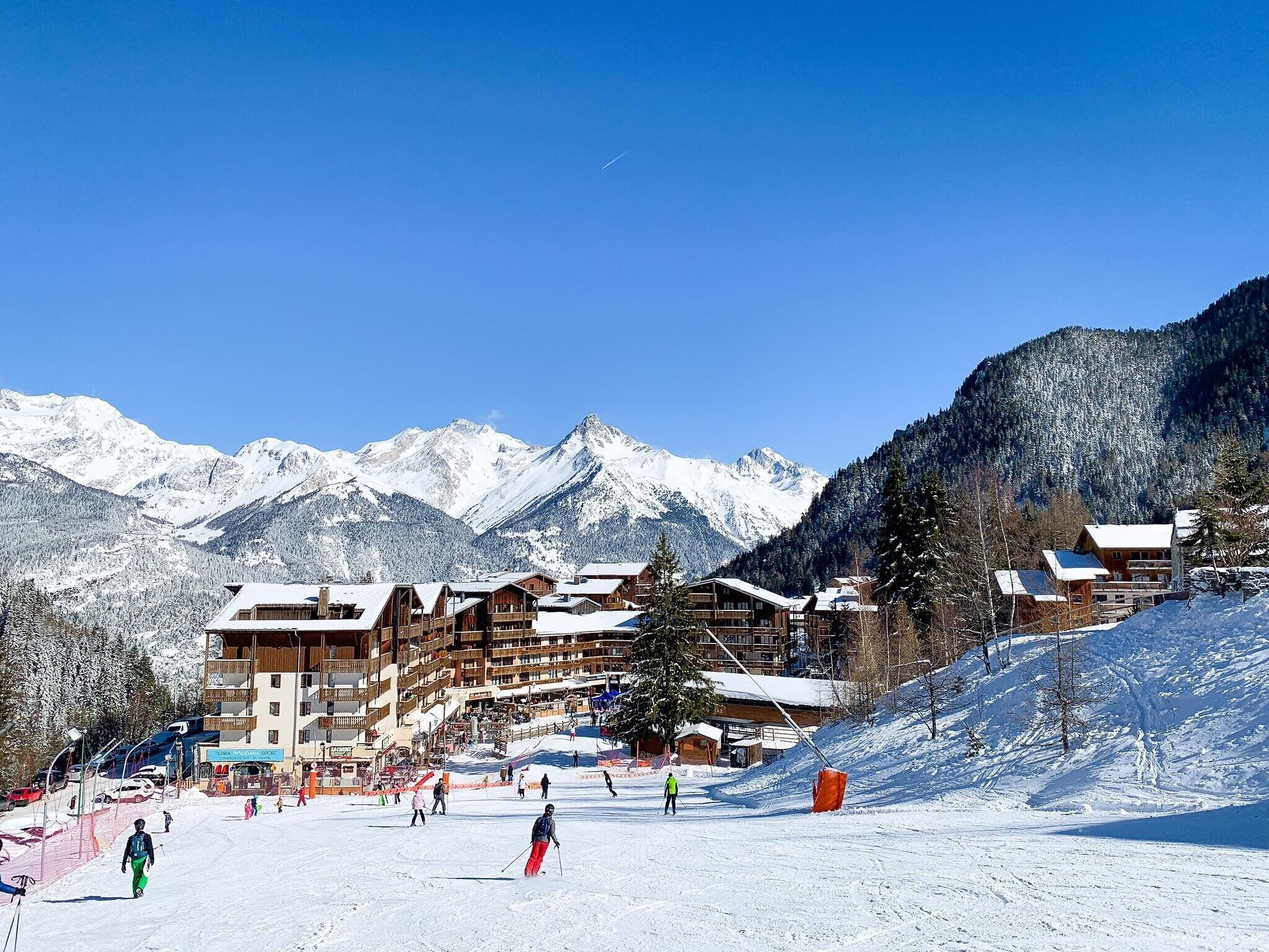 A ski resort with wooden lodges, a ski slope, and snow-covered mountains in the background.
