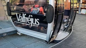 A cable car with 'Valfrejus' branding and a contact number, stationary on a platform with a metal grate floor. - Apartment 'Le Petit Bonheur' with Mountain View and Balcony (Modane)