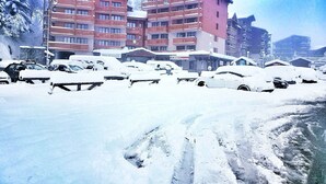 Un hôtel à plusieurs étages doté de balcons, un parking rempli de voitures et un paysage enneigé.