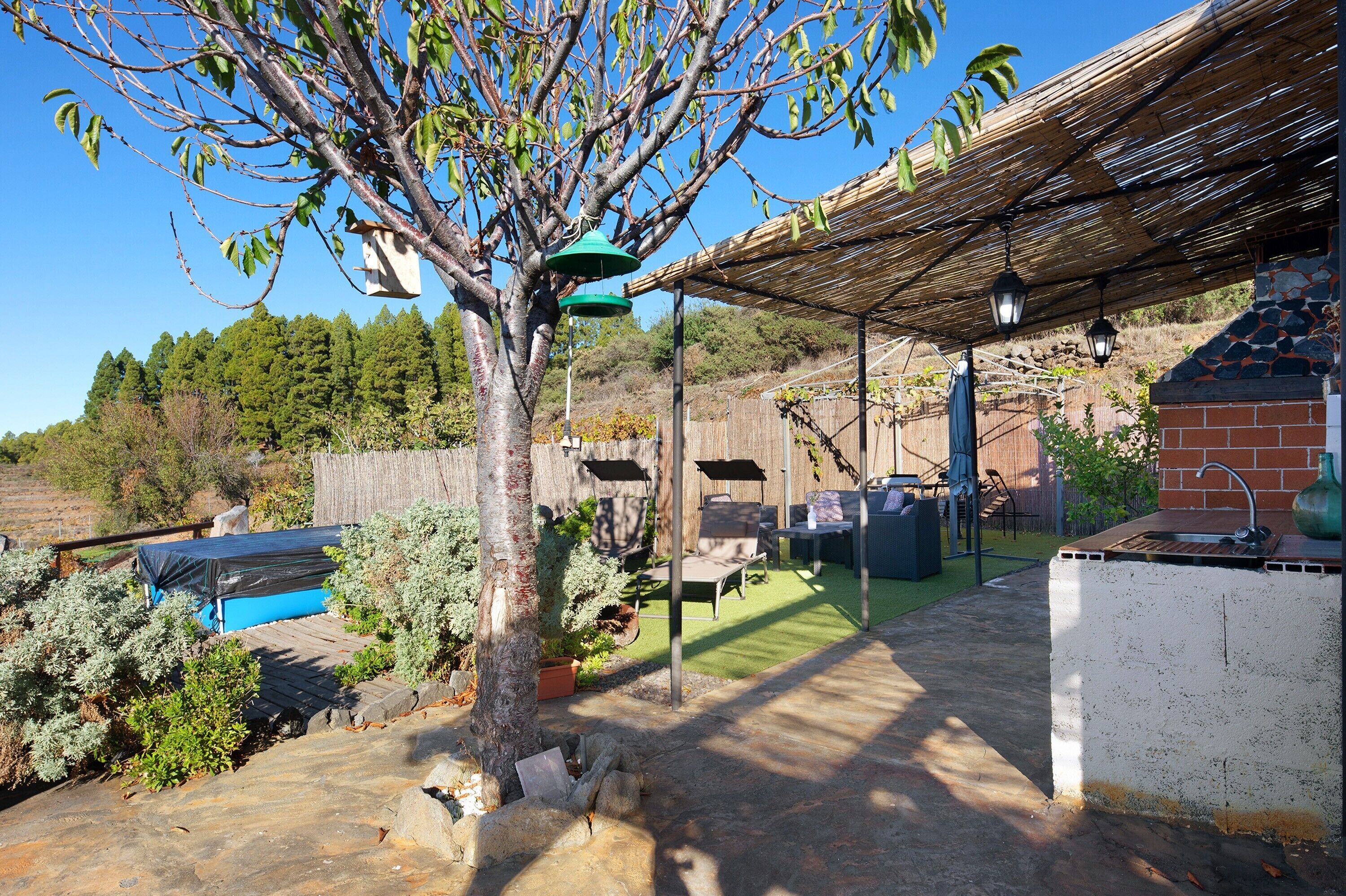 Un patio con una parrilla, mobiliario exterior y una pérgola que ofrece sombra.