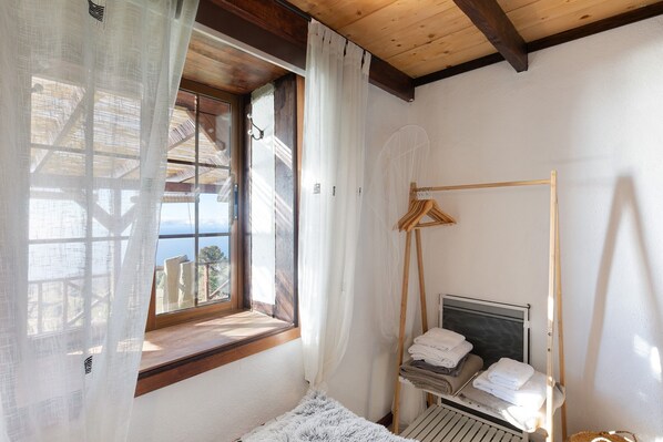 Ein Schlafzimmer mit Bett, einem Fenster mit Vorhängen, einer Holzbalkendecke und einem Nachttisch mit Handtüchern.