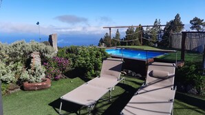 A backyard with a swimming pool, two lounge chairs, and a stone structure. - Holiday Home 'Media Pipa' with Sea View, Wi-Fi and Air Conditioning (Puntagorda)