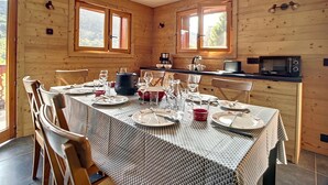 Een houten interieur met een eettafel voor vier personen, een keuken met een magnetron en grote ramen.