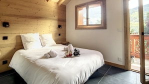 Een slaapkamer met houten lambrisering, een bed, kussens, een dienblad met handdoeken en mokken, en een raam met uitzicht.
