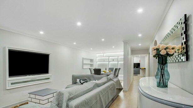 A modern bedroom with a bed, a TV, a desk, and a bathroom with a mirror and flowers.