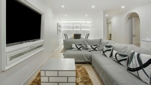A modern living room with a sectional sofa, a flat-screen TV, and recessed ceiling lighting.