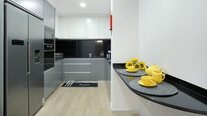A modern kitchen with stainless steel appliances, a black countertop, and a yellow tea set.