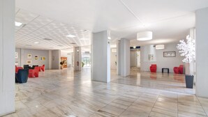 Um hall amplo com piso de azulejos, assentos vermelhos e um vaso de plantas.