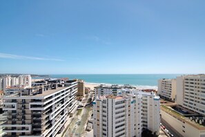 Un immeuble de grande hauteur doté de nombreux balcons, offrant une vue sur la plage et s’ouvrant sur un ciel dégagé.