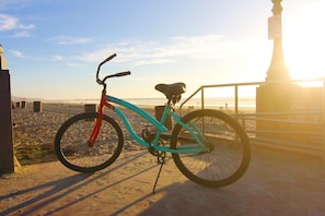 Ein Fahrrad steht auf einem sandigen Strand, im Hintergrund eine Brüstung und eine Statue.