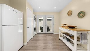 A kitchen with a white refrigerator, a washing machine, a wooden table with a bowl, and a shelf with dishes. - The Succulent House, parking, walk to Bay! (San Diego)