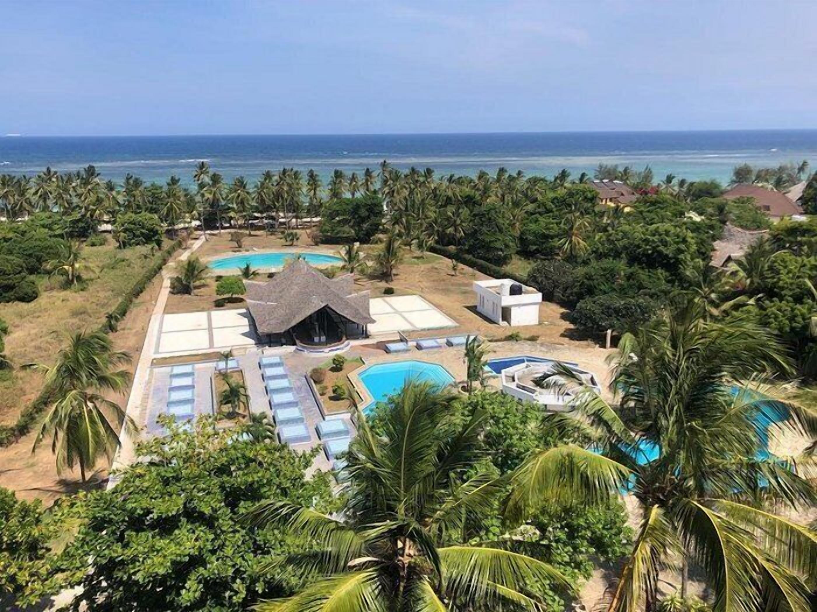A resort with multiple swimming pools, a central building, and a view of the ocean.