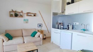 A living room with a beige sofa, a wooden coffee table, and a kitchen area with white cabinets and a sink.