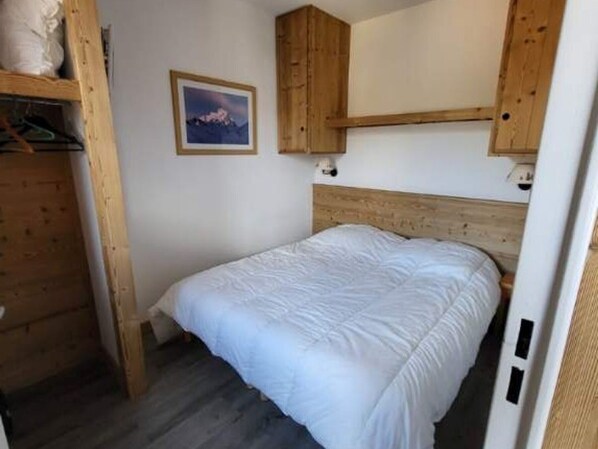 A bedroom with a wooden headboard, a bed with white bedding, a framed picture on the wall, and a wooden shelf above the bed. - Comfortable 2-room, balcony and ski locker (Le Dévoluy)