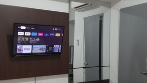 A hotel room with a mounted TV displaying various streaming services, a wooden cabinet below, and a door leading to another room.