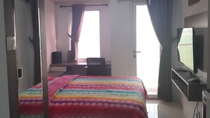 A hotel room with a bed, a desk, a chair, an air conditioning unit, and a television.