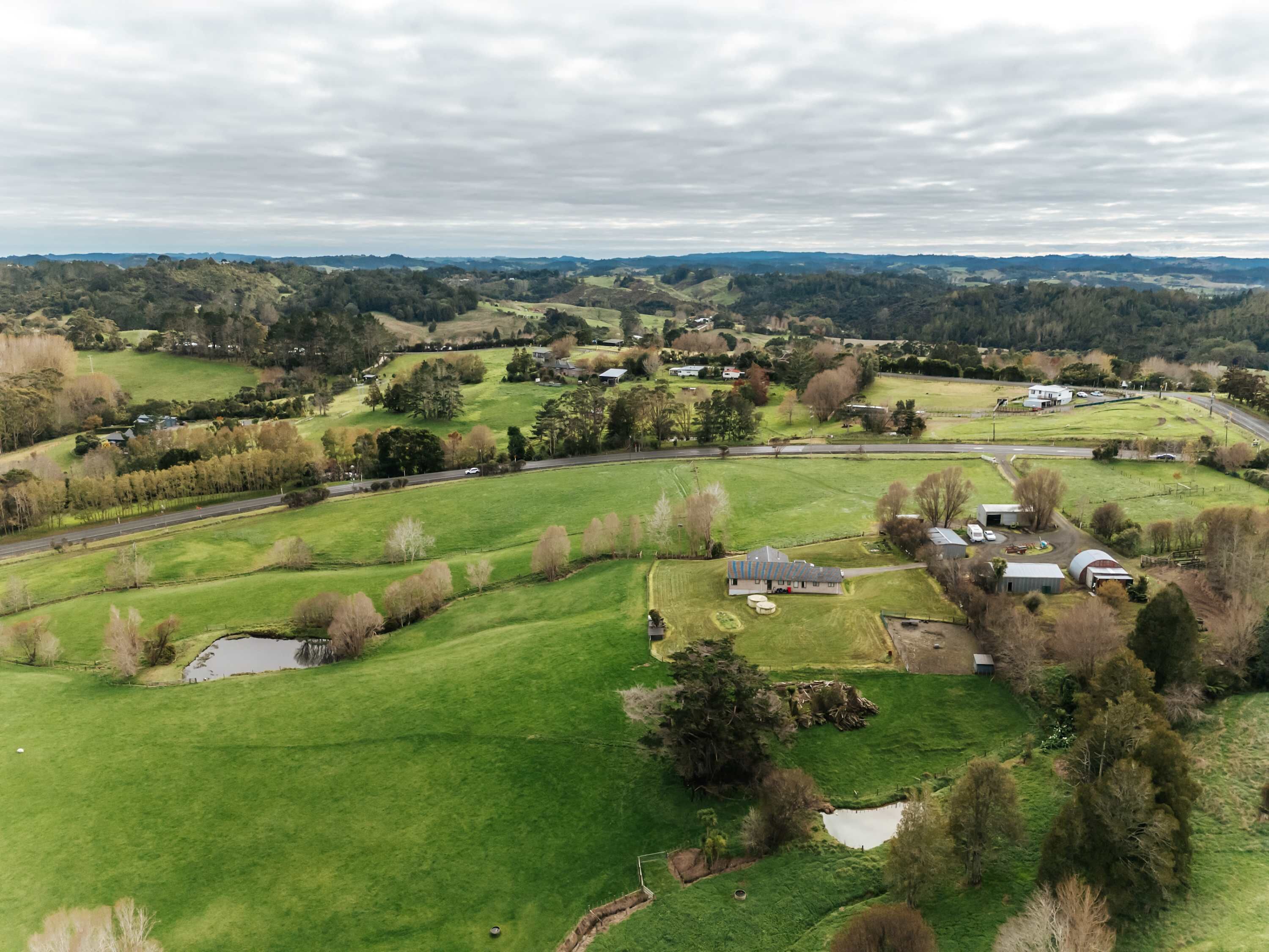 Luchtbeeld van een landelijk gebied met groene velden, verspreide bomen en enkele gebouwen.