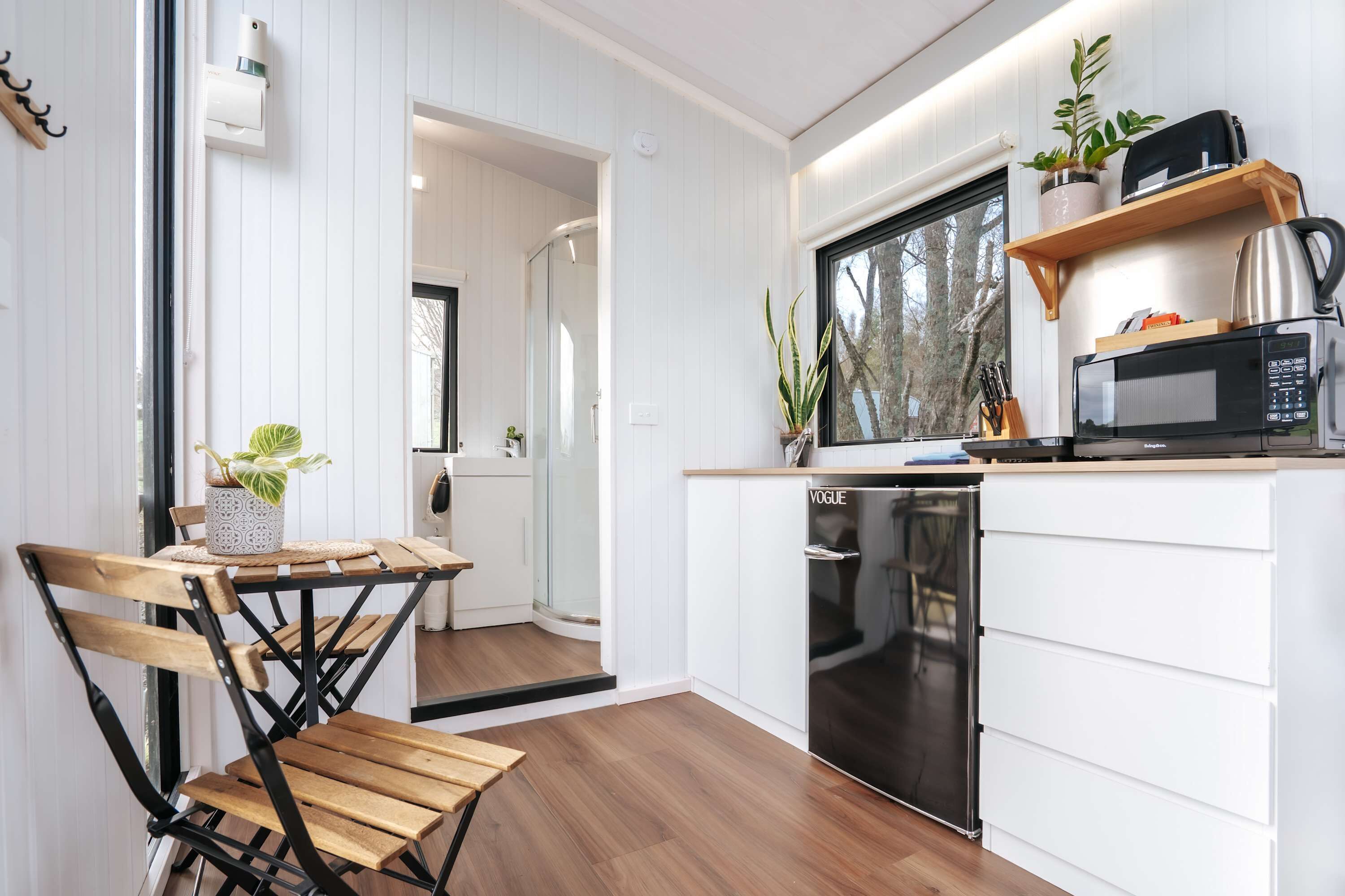 A modern kitchen with white cabinetry, a built-in microwave, and a window overlooking a forest.