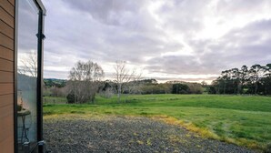 A view from a building's interior looking out to a grassy field with trees and a cloudy sky.