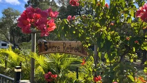 A wooden sign with '5 Acre Retreat' written on it, surrounded by lush greenery and pink flowers.