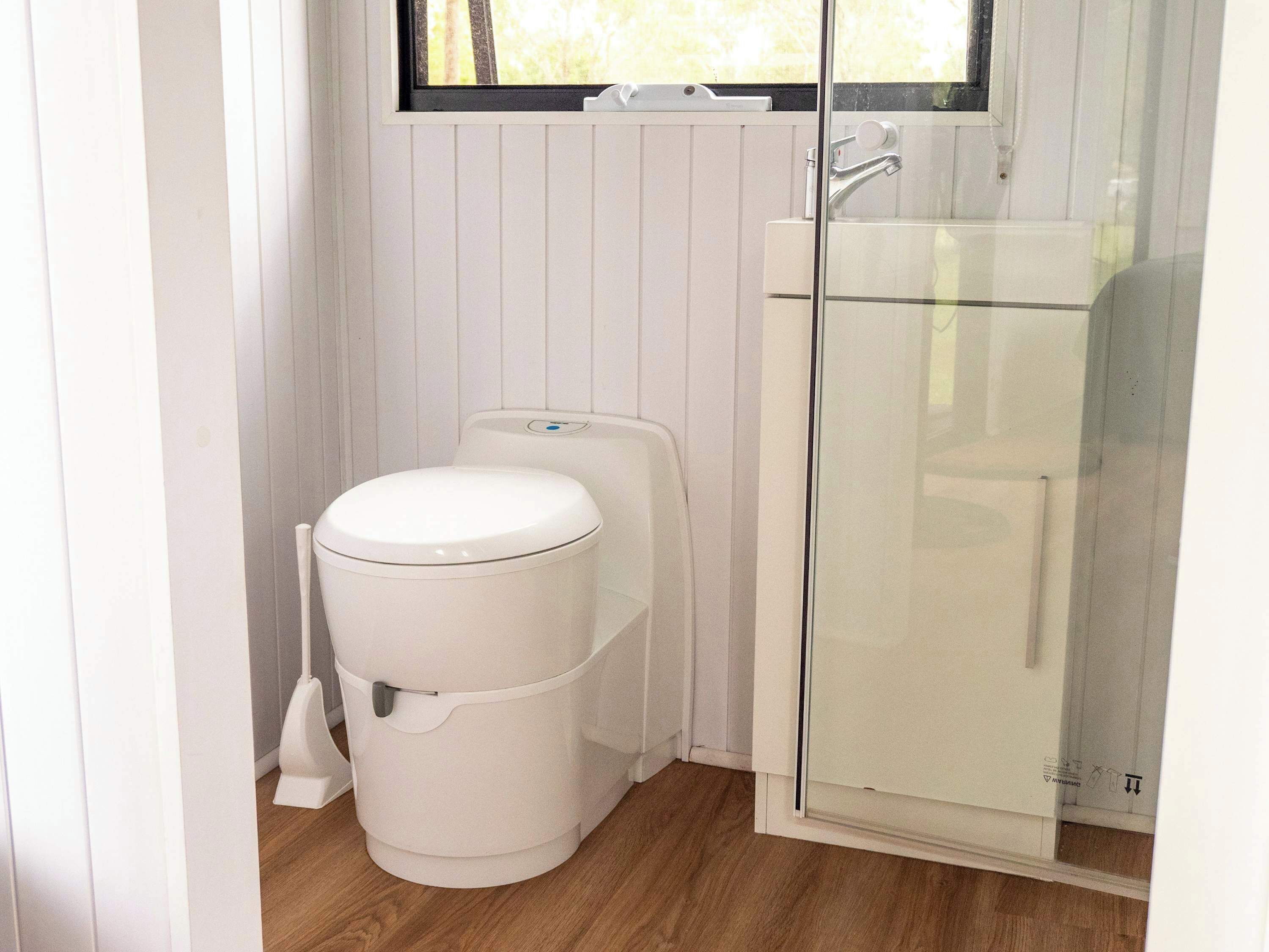 Un bagno compatto con il water bianco, un box doccia in vetro e una finestra sopra il lavandino.