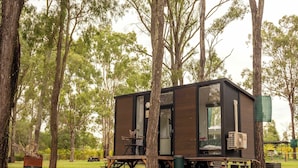 A small cabin with a table and chairs outside, surrounded by trees.
