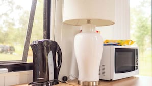 A kitchen area with a black electric kettle, a white lamp, and a white microwave on a wooden countertop.