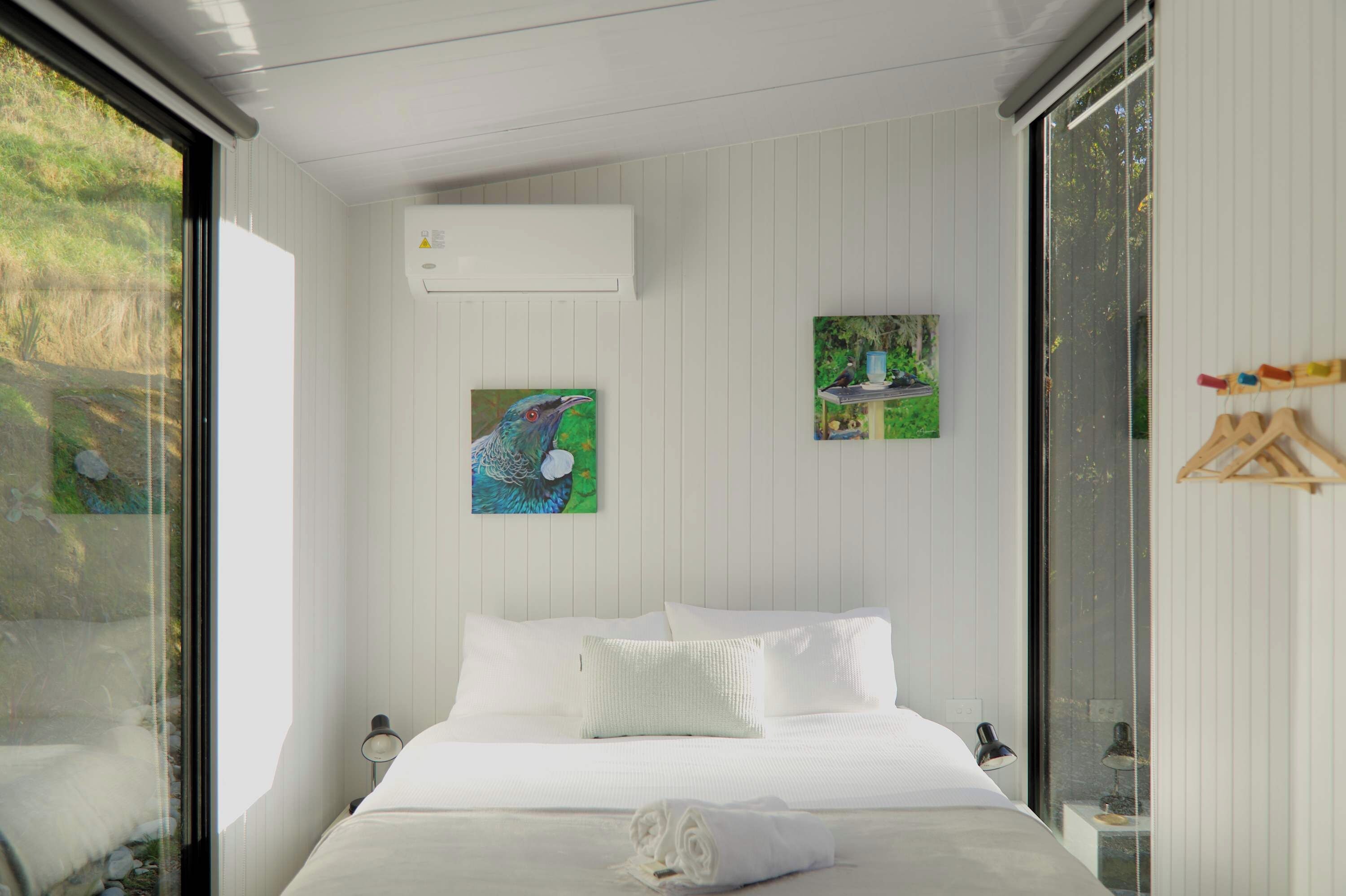 A modern bedroom with a large bed, white walls, and a window overlooking greenery.
