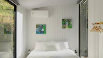 A modern bedroom with a large bed, white walls, and a window overlooking greenery.