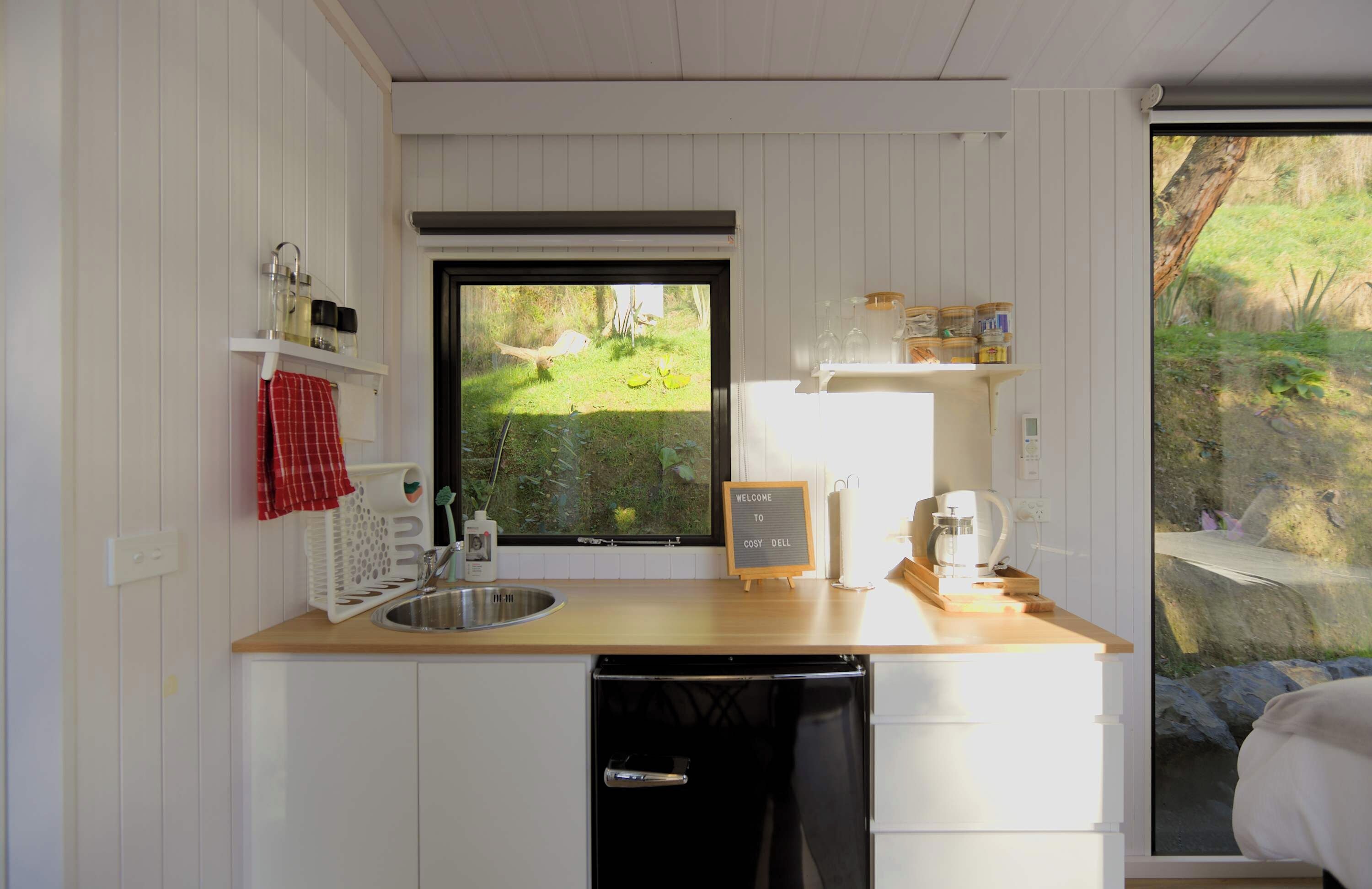 Een kleine keuken met een houten aanrecht, een spoelbak, een vaatwasser en een raam met uitzicht op een tuin.