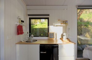 Een kleine keuken met een houten aanrecht, een spoelbak, een vaatwasser en een raam met uitzicht op een tuin.