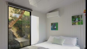 A bedroom with a large window, a bed with white linens, and a painting on the wall. - Cosy Dell Tiny House (Herbert)