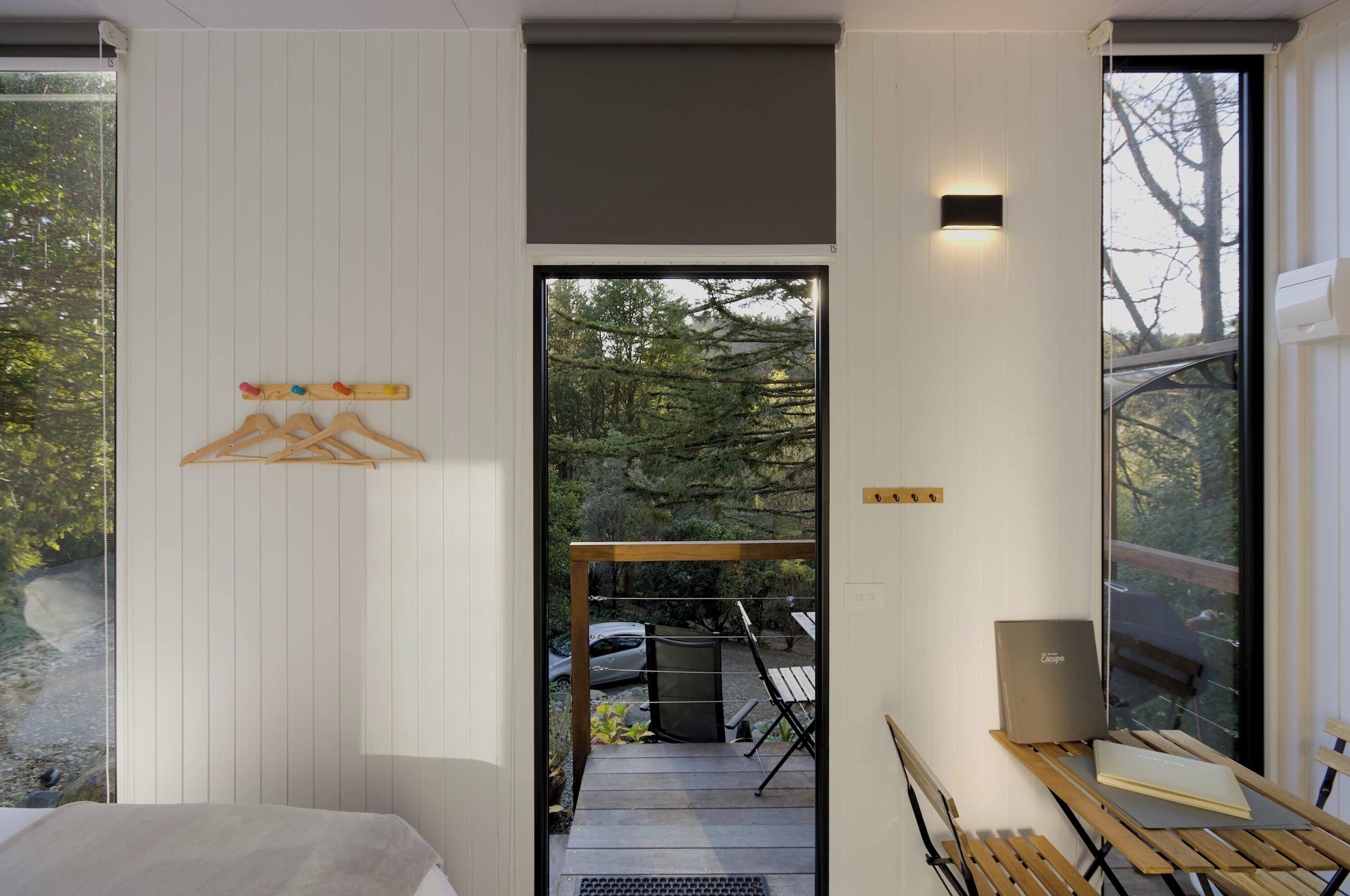 Een moderne kamer met een bed, een houten tafel met een laptop en uitzicht op een tuin door een glazen deur.