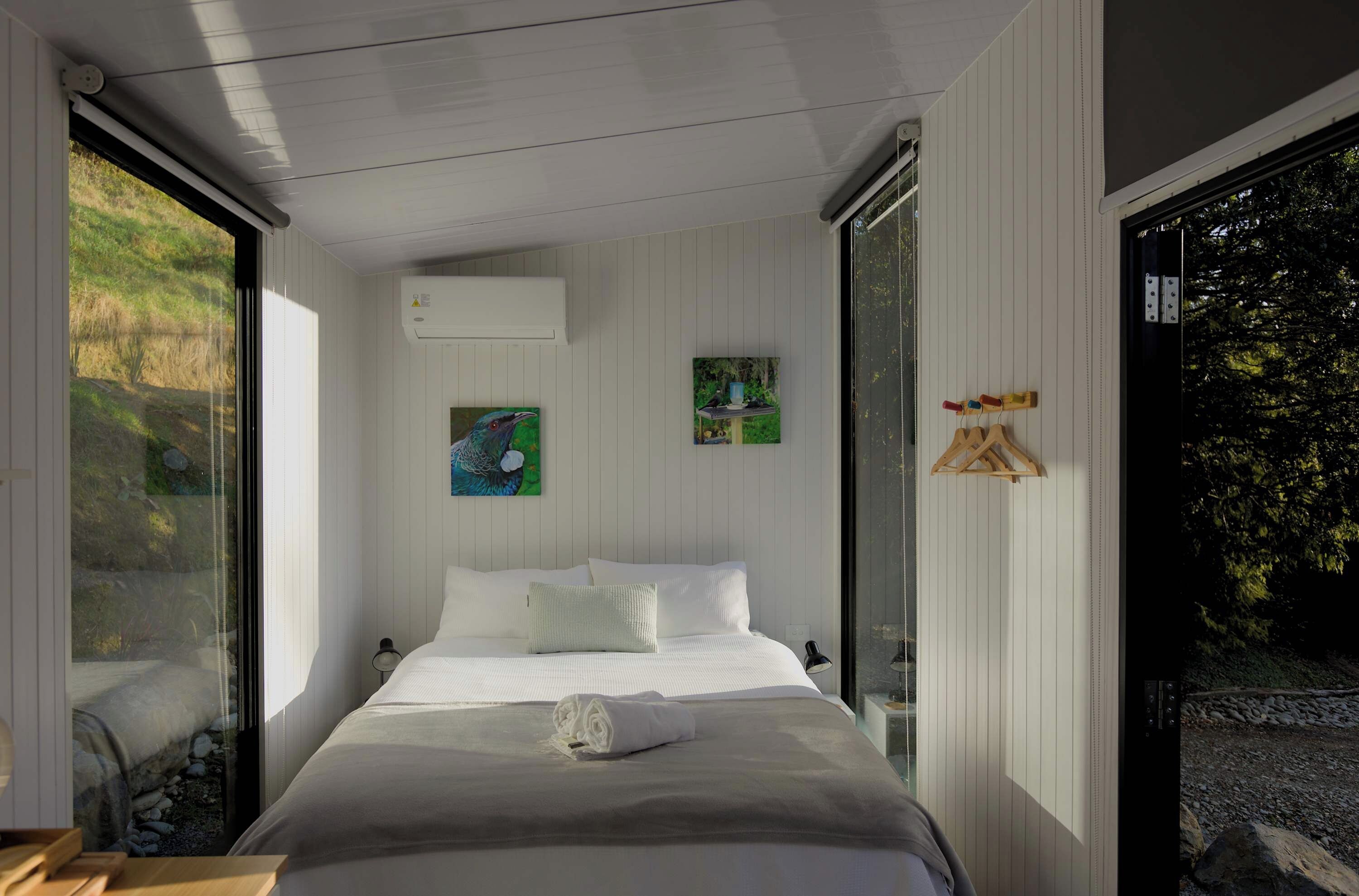 Un dormitorio moderno con una cama grande, paredes blancas y vistas a un jardín a través de una puerta corrediza.