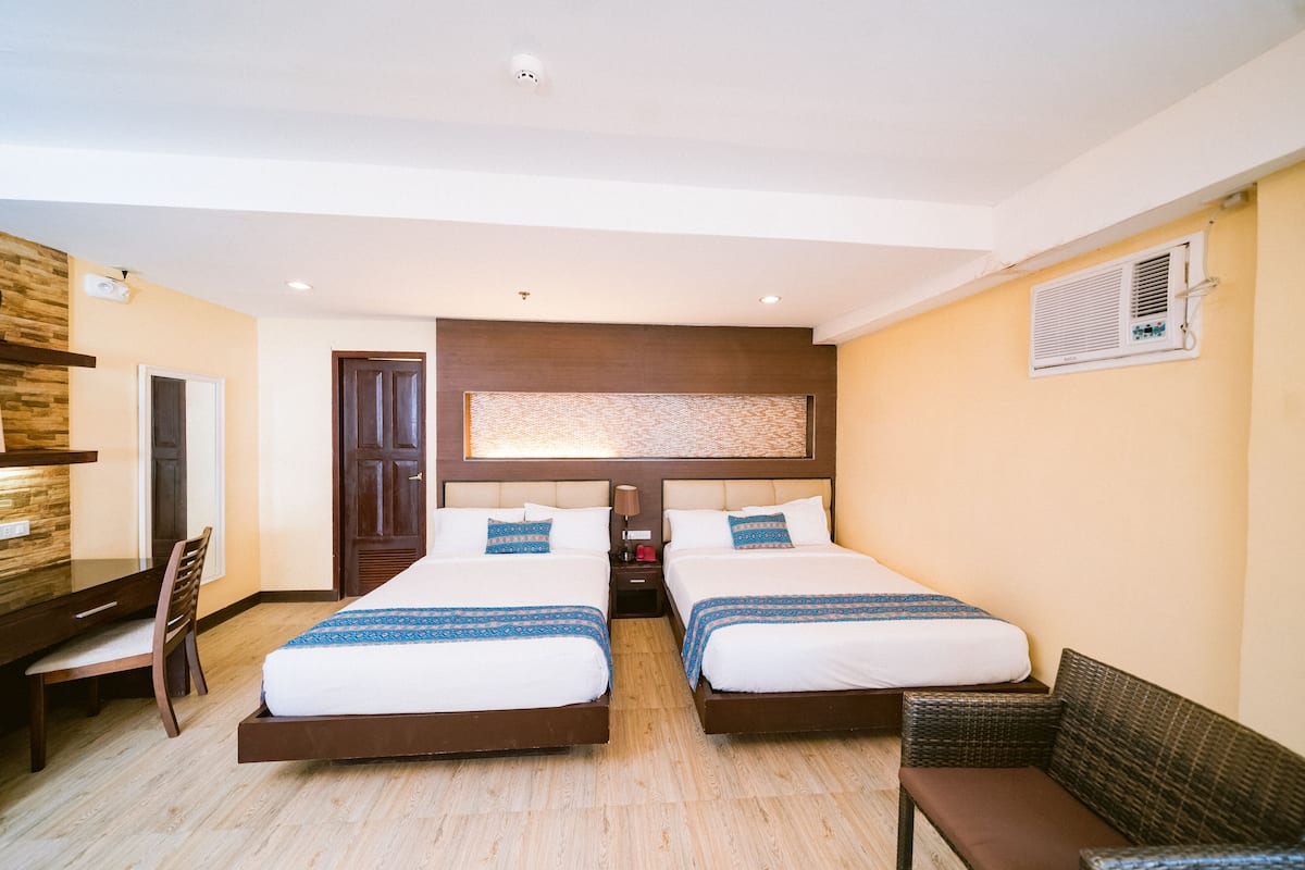 A hotel room with two beds, a desk, a chair, and a sofa.