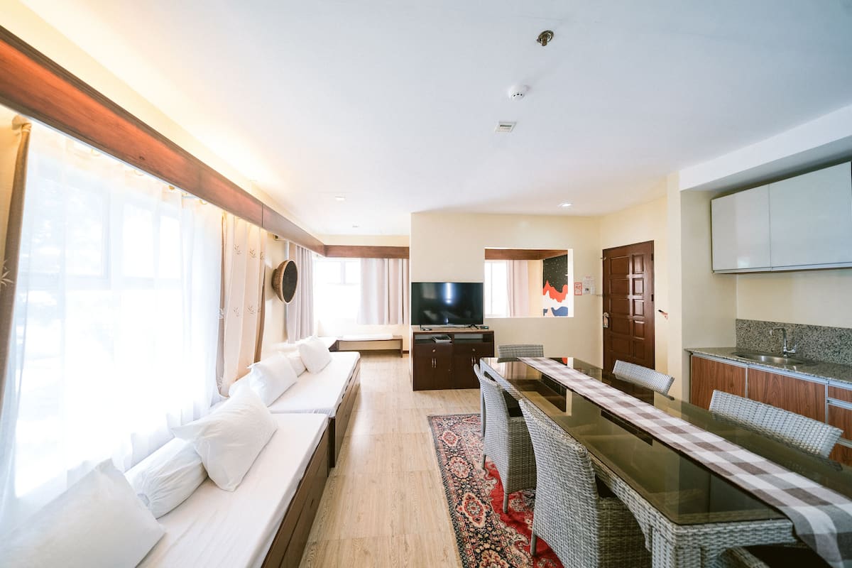 A modern living room with a sofa, TV, dining table, and kitchen area.