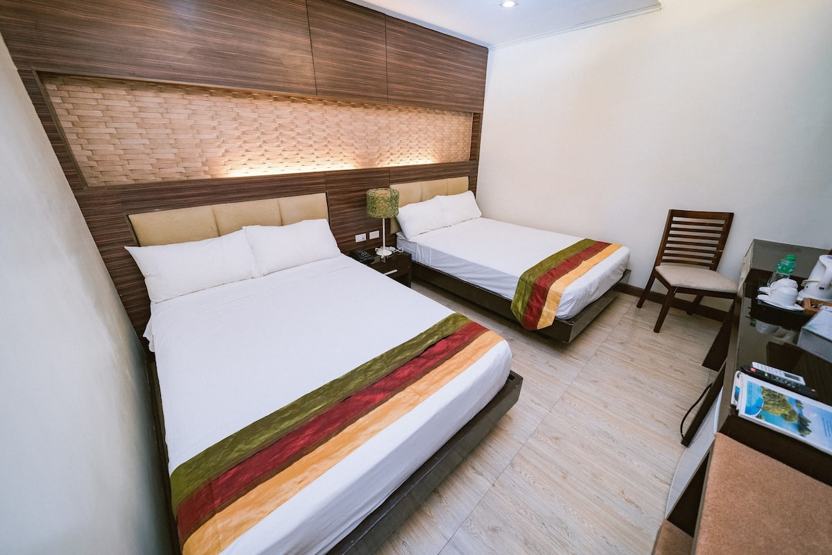 A hotel room with two beds, a wooden headboard, a desk, and a chair.