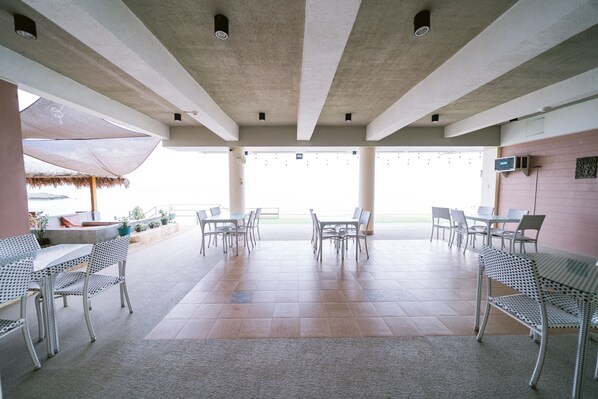 A spacious outdoor dining area with metal tables and chairs, a concrete ceiling, and a view of the sky.