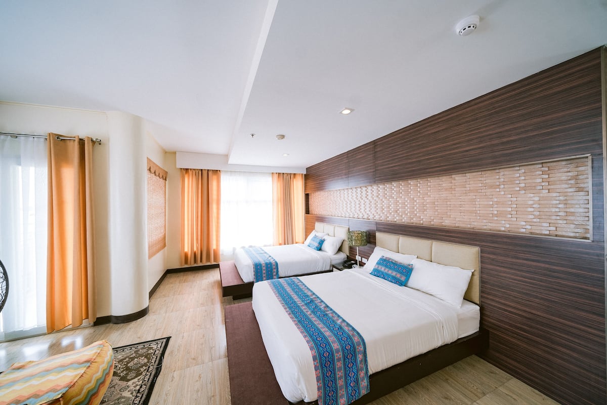 A hotel room with two beds, a wooden headboard, a brick-patterned wall, and a large window with curtains.
