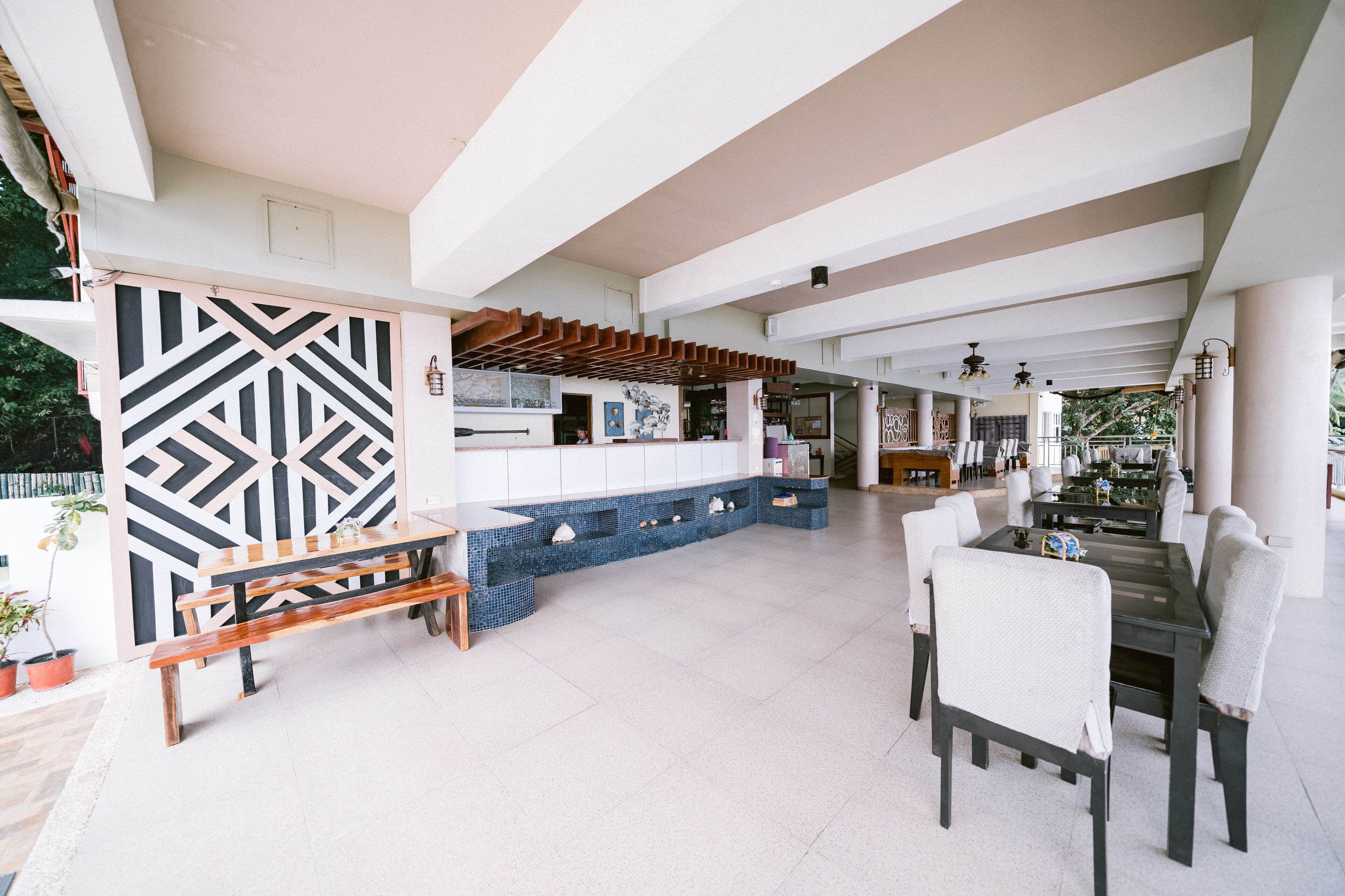 A spacious indoor area with a long bench, a dining table with chairs, and a blue tiled bench along the wall.