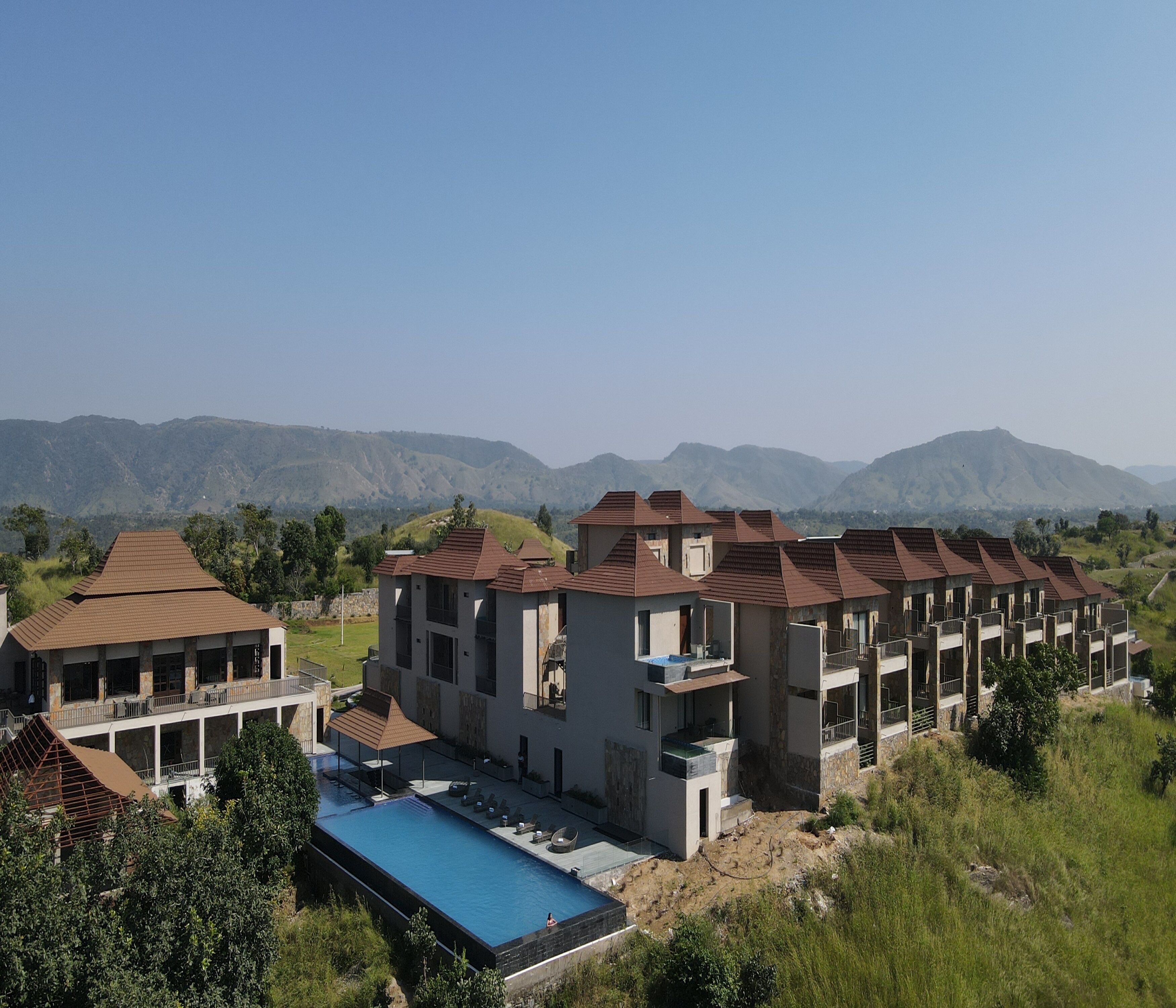 A resort with multiple buildings, a swimming pool, and a mountainous backdrop.