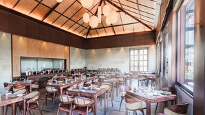 A spacious dining area with multiple tables and chairs, a high ceiling with hanging light fixtures, and large windows allowing natural light. - Sajjan Bagh Resort Kumbhalgarh (Kumbhalgarh)