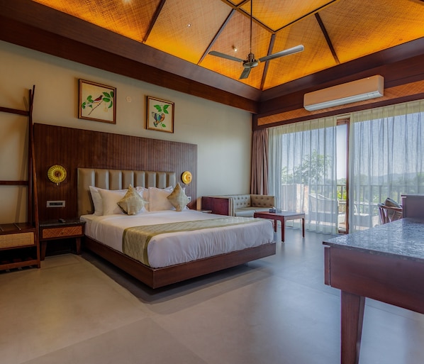 Un dormitorio espacioso con una cama grande, ventilador de techo y vistas al exterior a través de amplias ventanas.