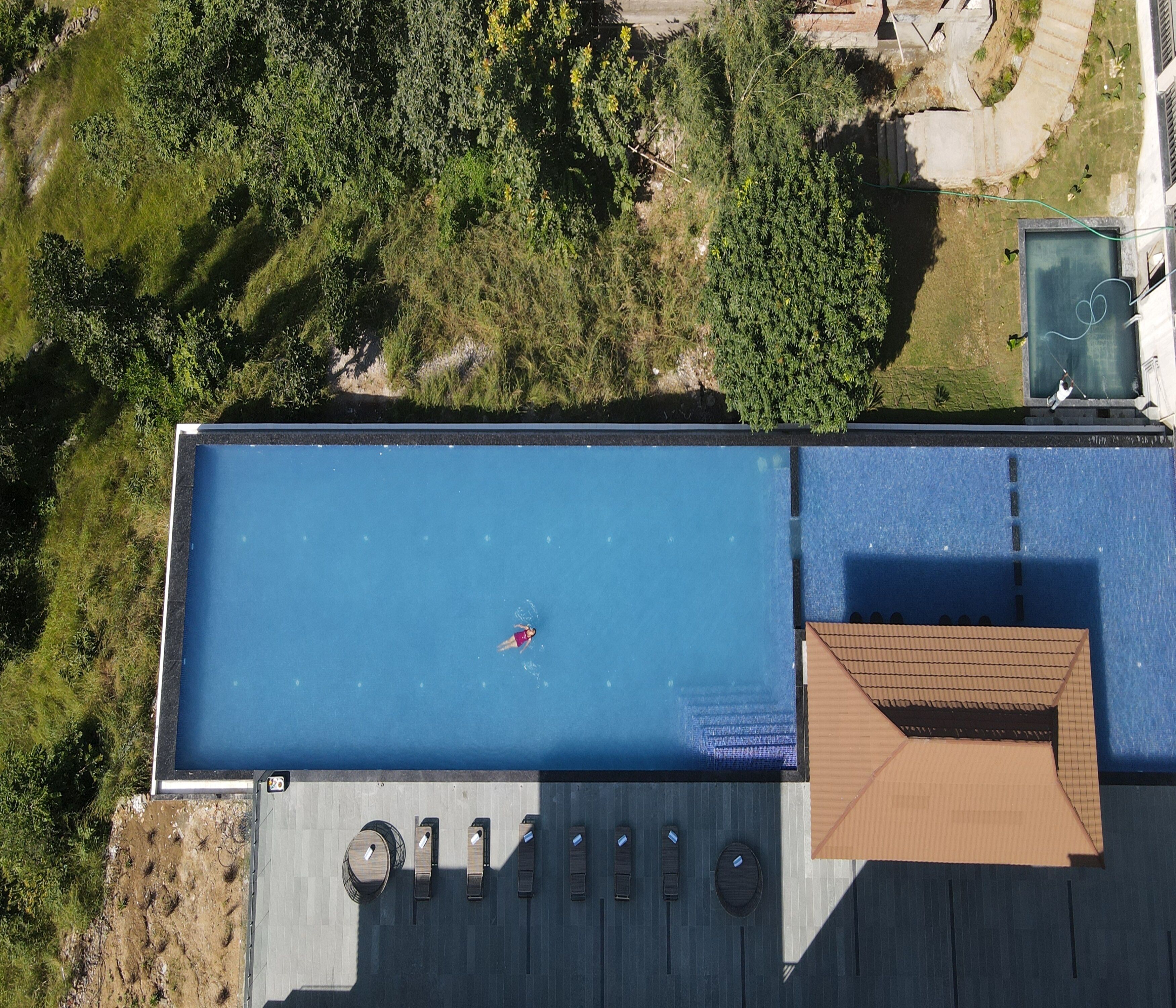 Eine Vogelperspektive zeigt einen Dachpool mit einer Person, die schwimmt, umgeben von Grünpflanzen und einem Gebäude mit Dach.
