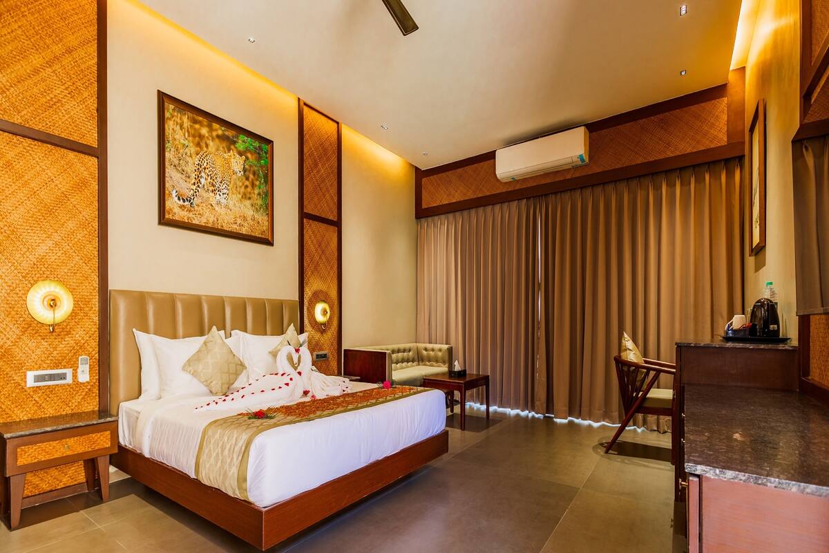 A hotel room with a large bed, a desk, a chair, a wall-mounted air conditioner, and a painting on the wall.