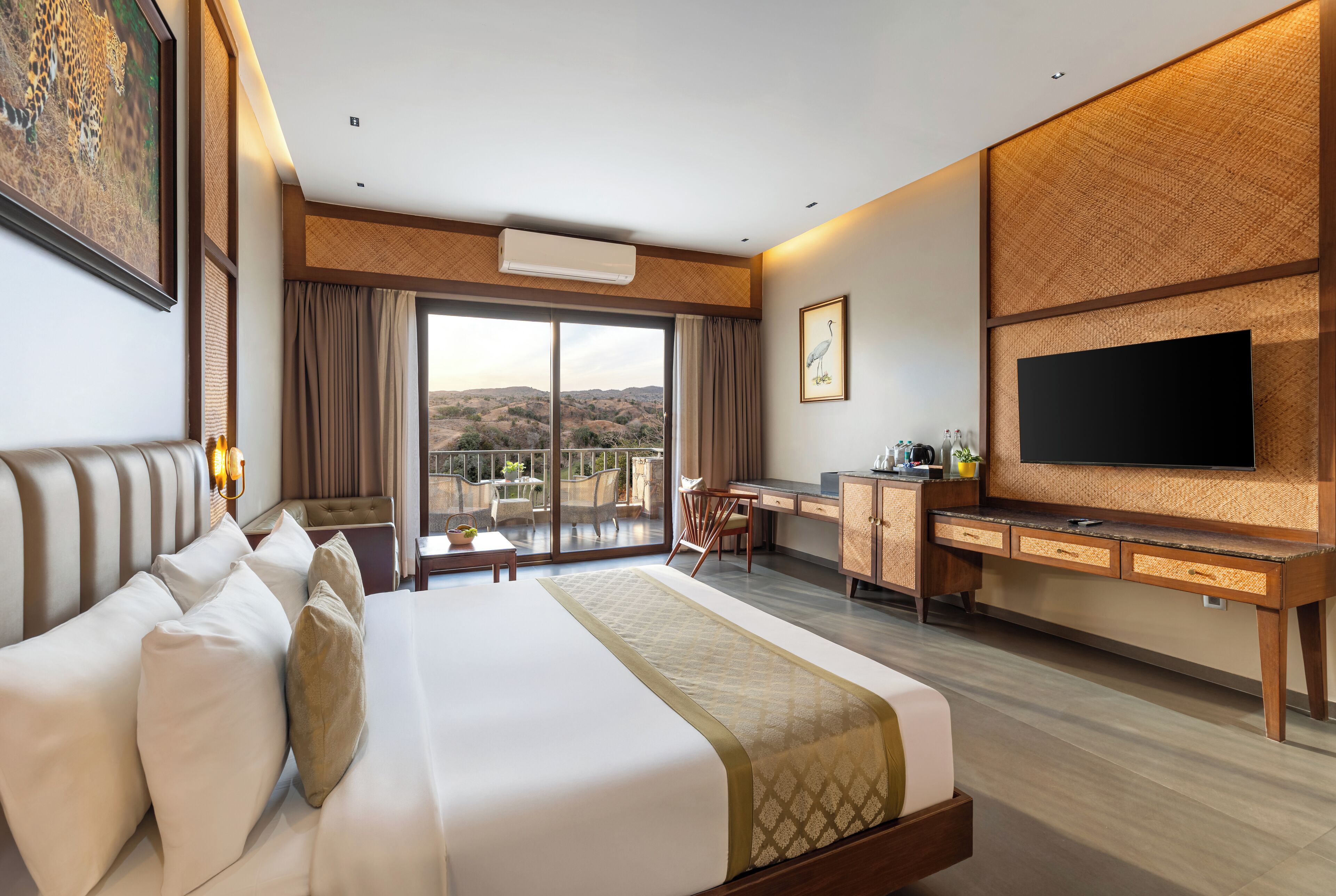 A hotel room with a large bed, a desk, a television, and a balcony with a view of the hills.